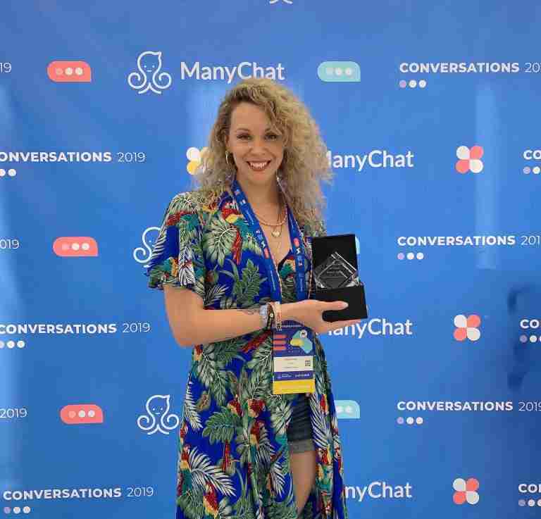 Angela Allan with her Emerging Agency Award in front of a Manychat media wall at Conversations conference in Austin Texas in 2019